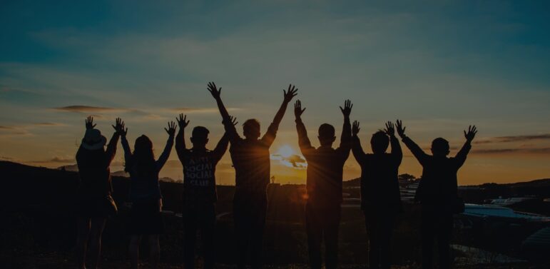 A group of people holding their hands in the sky in front of a sunset